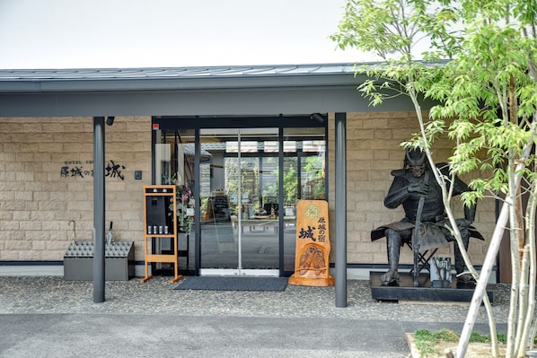 A hotel entrance with a glass door, a wooden signboard, and a statue of a samurai.