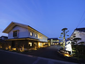 A traditional Japanese hotel with a two-story structure, a well-lit entrance, and a stone lantern.