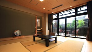 Ein Raum mit Tatami-Matten, einem niedrigen Tisch, einem Stuhl und einer Holzskulptur.