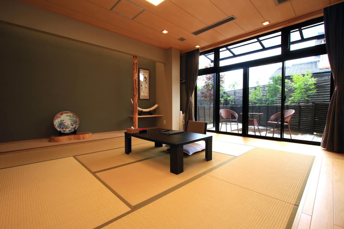 Ein Raum mit Tatami-Matten, einem niedrigen Tisch, einem Stuhl und einer Holzskulptur.