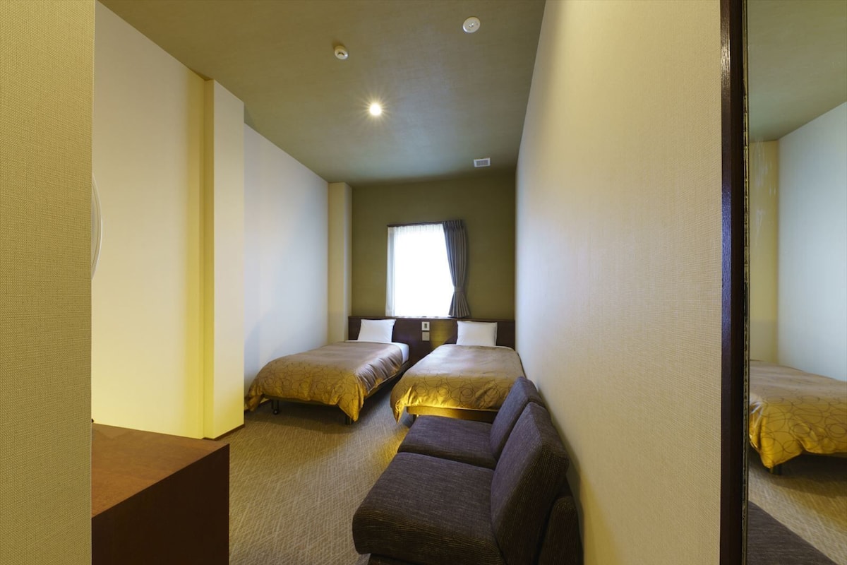 Ein Hotelzimmer mit zwei Betten, einem Sofa und einem großen Fenster mit Vorhängen.