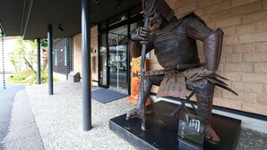 Eine Samurai-Statue in Rüstung vor einem Gebäude mit Backsteinmauer und Glastür.
