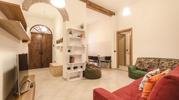 A living room with a red sofa, a wooden bookshelf, a dining table with chairs, and a wooden door. - Appartamento Schiavonia (Bologna)
