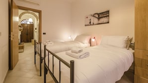 A hotel room with two beds, a wooden wardrobe, a painting on the wall, and a hallway leading to another room. - Appartamento Schiavonia (Bologna)