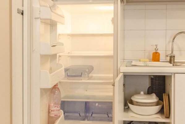 A kitchen with a built-in refrigerator, a sink, and a shelf with a colander and a bottle.