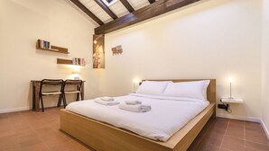 A bedroom with a wooden bed, two chairs, a small table, and a wall-mounted shelf with books. - Ca' di Leo (Bologna)