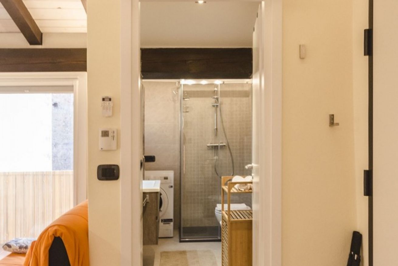 A compact bathroom with a shower, a toilet, and a washing machine.