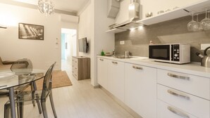 A modern kitchen with white cabinets, a microwave, and a glass dining table. - Le Torri Suite (Bologna)