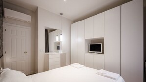 A modern bedroom with a bed, a TV mounted on the wall, a wardrobe, and a mirror.
