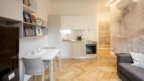 A modern kitchen with white cabinets, a dining area with a white table and chairs, and a grey sofa in a living area with a herringbone wood floor.