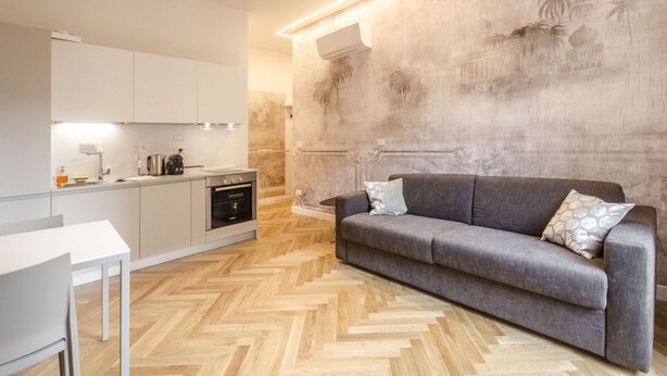 A modern kitchen with a herringbone floor pattern, a grey sofa with patterned cushions, and a wall mural depicting palm trees and buildings.