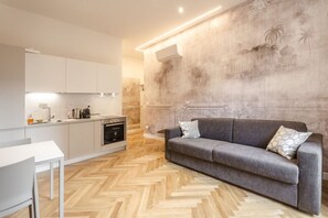 A modern kitchen with a herringbone floor pattern, a grey sofa with patterned cushions, and a wall mural depicting palm trees and buildings. - Calzolerie Apartment (Bologna)