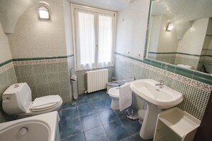 A bathroom with a toilet, bidet, sink, and a window with curtains. - Garisenda Lodge (Bologna)