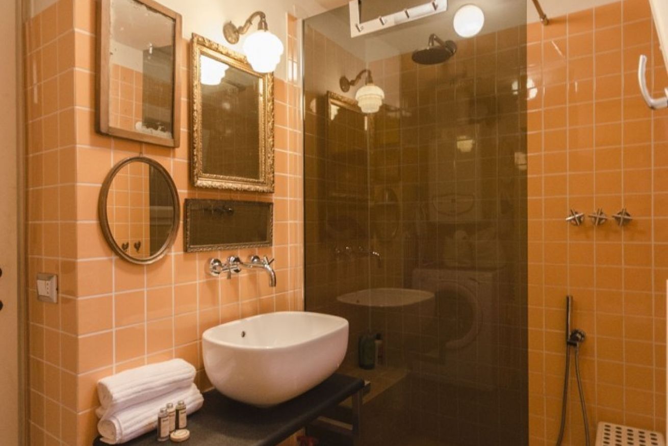 A bathroom with a white sink, two mirrors, a shower, and orange-tiled walls.
