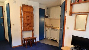 Une pièce de taille modeste comprenant un lit, une petite table en bois, un téléviseur posé sur un meuble, un coin cuisine et une salle de bain.