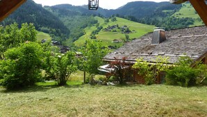 Uma chalé tradicional com telhado inclinado, um lança-luz pendurado e vista para um vale com casas e vegetação.