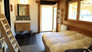 Quarto com cama, escada de madeira, banheiro com pia e espelho, e janela com vista.