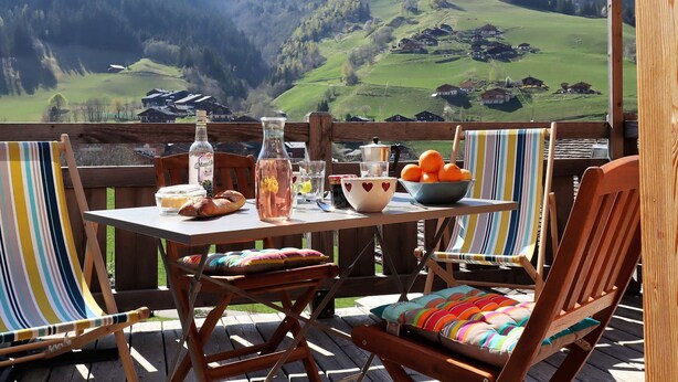 Um deck de madeira com uma mesa posta para refeição, com vista para uma paisagem montanhosa.