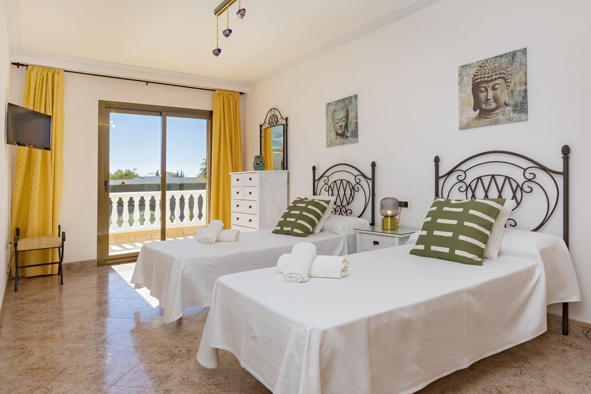 Habitación de hotel con dos camas, televisión, balcón y obras de arte en las paredes.