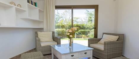 A room with wicker furniture, a glass-top table, and a view of greenery outside.