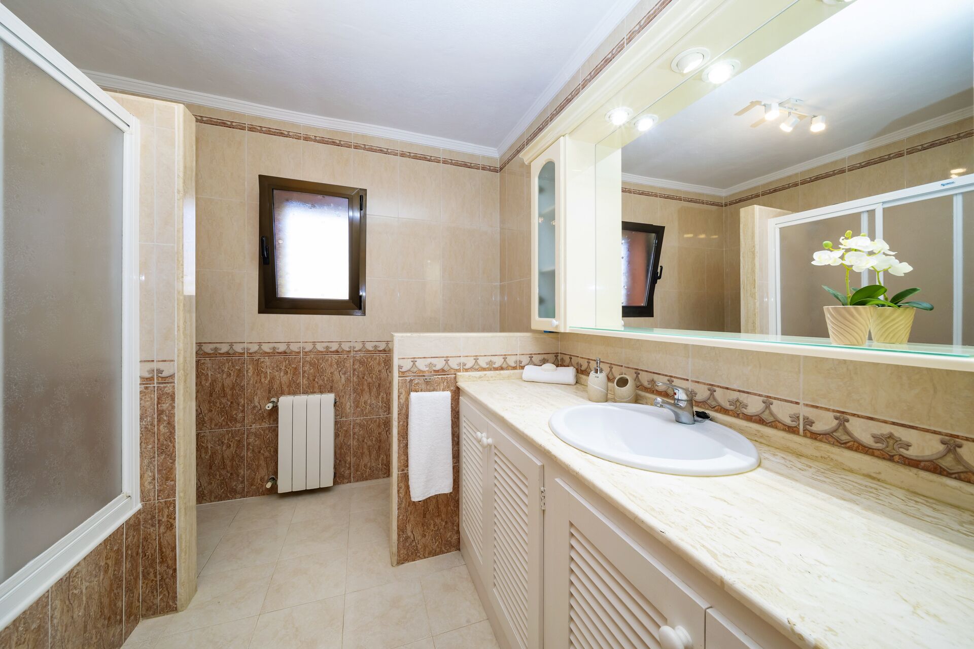 A bathroom with a large mirror, a sink, a towel rack, and a radiator.