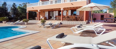 A poolside area with lounge chairs, a pool, and a building with a balcony.