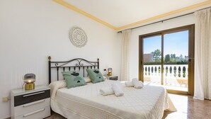 A bedroom with a bed, two bedside tables, a nightstand, a decorative wall piece, and a balcony with a view.