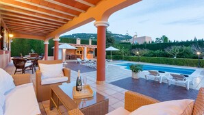 An outdoor patio with wicker furniture, a pool, and a view of a hillside.