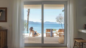 A room with a sliding glass door leading to a deck with a view of the sea and mountains.