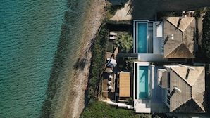 An aerial view of a modern resort with a pool, a beach, and a mountain backdrop.