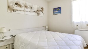 Ein Schlafzimmer mit einem großen Bett, einem Nachttisch mit Lampe, einem Wandbild und einem Fenster mit Vorhängen.