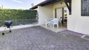Eine Terrasse mit Grill, weißen Plastikstühlen und einem Tisch.