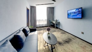 A modern hotel room with a sofa, a small table with a plant, a desk, and a TV mounted on the wall. - W Kardon Hotel (Guangzhou)