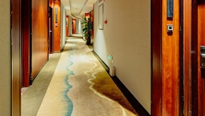 A hotel corridor with wooden doors, numbered room signs, and a carpet with a wave pattern. - W Kardon Hotel (Guangzhou)