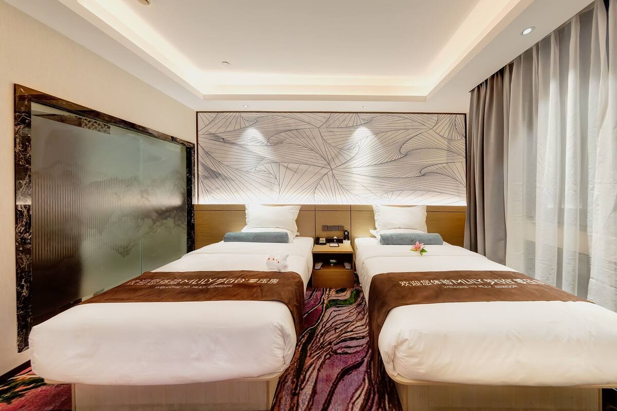 Une chambre d’hôtel avec deux lits, un grand miroir, un mur décoratif et une table de chevet avec une lampe.