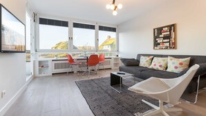 En moderne stue med en grå sofa, en hvid stol og et spiseområde med røde stole.