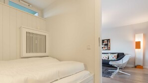 Et soveværelse med seng, radiator, en grå sofa, en lampe og en bogreol.