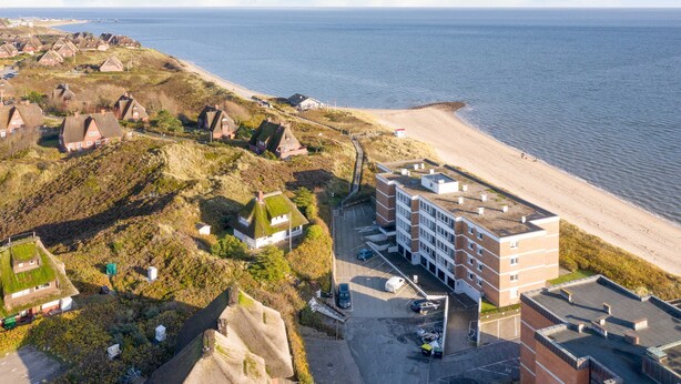 Oversigtsbillede af et kystområde med traditionelle huse, en strand og en moderne bygning med parkering.