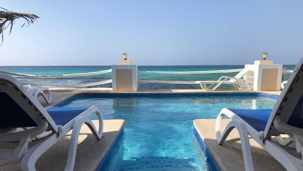 A pool area with two lounge chairs facing the ocean, a clear view of the sea, and a tiled pool. - Fantastic apartment in Montego Bay (Montego Bay)