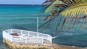 A white wooden deck with a stone wall foundation extending into clear turquoise water. - Fantastic apartment in Montego Bay (Montego Bay)