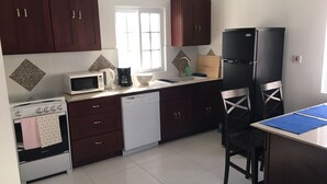 A compact kitchen with dark wooden cabinets, a white stove, a dishwasher, a black refrigerator, and a dining table with chairs. - Fantastic apartment in Montego Bay (Montego Bay)