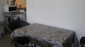 A small kitchen with a microwave, sink, and a table with a tablecloth. There are chairs around the table. - Appart Hotel de la Paix (Barcelonnette)
