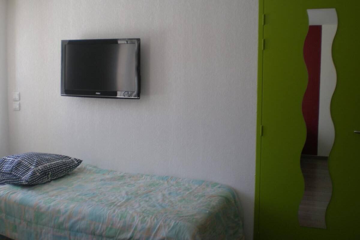 A bedroom with a bed, a television mounted on the wall, and a green door.