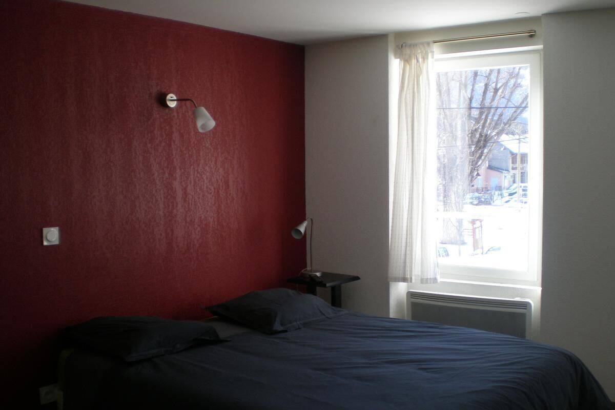A bedroom with a bed, a nightstand, a lamp, and a window with a view of the outside.