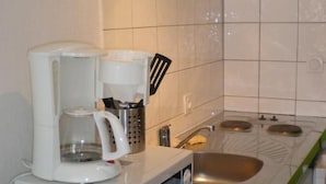 A compact kitchen with a microwave, coffee maker, and a sink. - Appart Hotel de la Paix (Barcelonnette)
