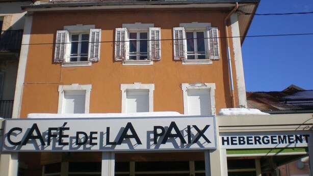 A building with a sign reading "CAFÉ DE LA PAIX" and another sign "HEBERGEMENT" below it. - Appart Hotel de la Paix (Barcelonnette)