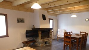 Ein Wohnzimmer mit Kamin, einem an der Wand montierten Fernseher, einem Esstisch mit Stühlen und einer Bank.