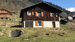 Eine Holzhütte mit Balkon, eingebettet in eine Berglandschaft, im Hintergrund weitere Gebäude.