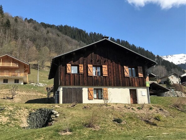 Un chalet en bois doté d’un balcon, situé dans une région montagneuse, avec d’autres bâtiments visibles à l’arrière-plan.