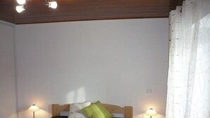 Een slaapkamer met een enkel bed, twee nachtkastjes met lampen, een houten hoofdbord en een raam met een witte gordijn.